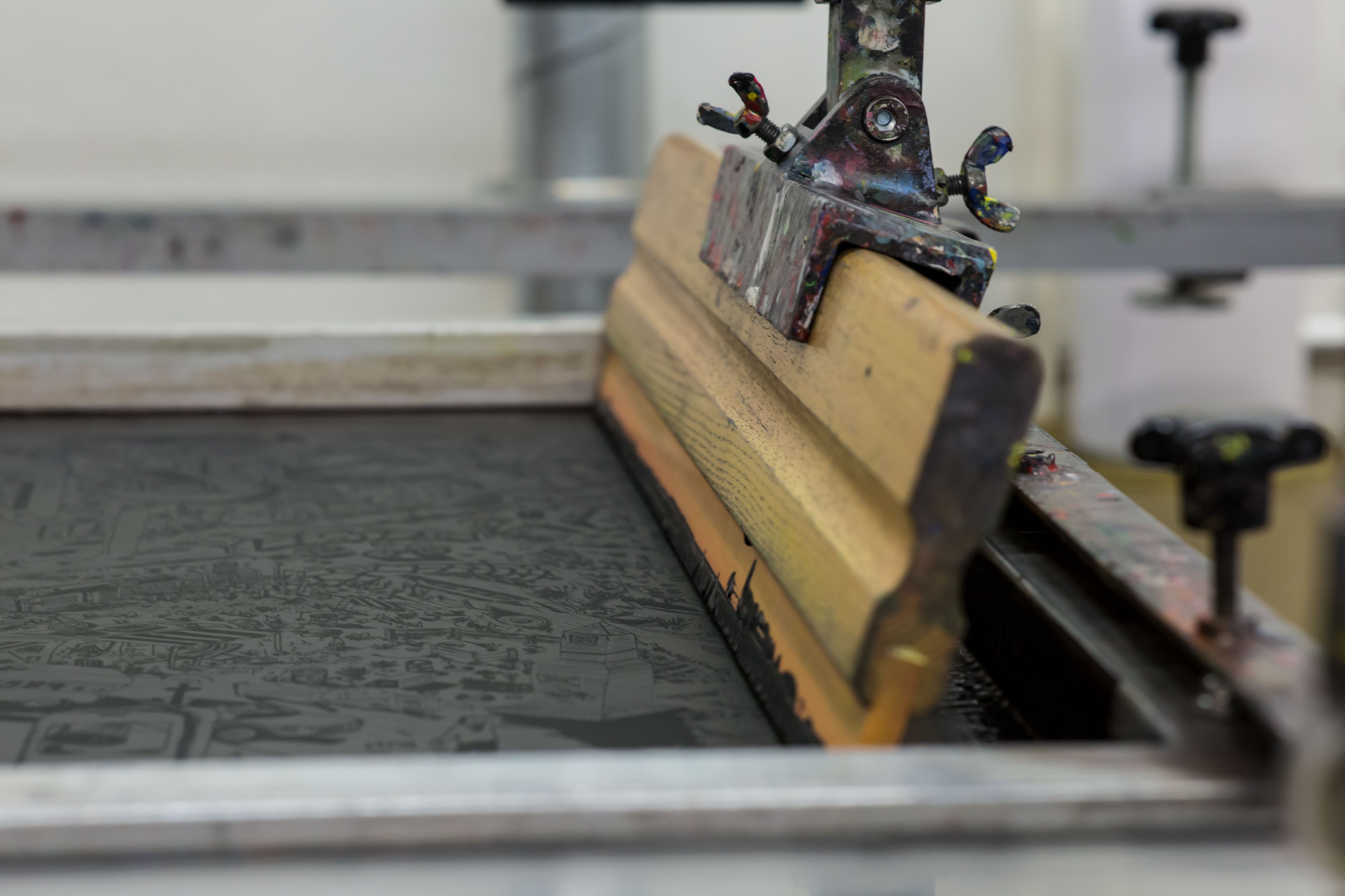 Racletă de serigrafie aplicând cerneală printr-o sită de imprimare